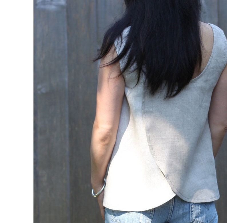May include: A light gray linen sleeveless top with a curved hemline. The top is made of a soft, breathable fabric and has a relaxed fit.