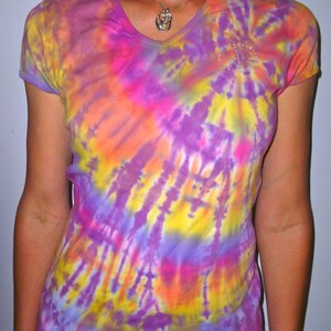 May include: A tie-dye shirt with a peace sign made of rhinestones. The shirt is a blend of purple, pink, yellow, and orange.