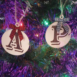 May include: Two wooden Christmas ornaments with the letters "A" and "P" on them. The ornaments are decorated with red and black checkered bows.