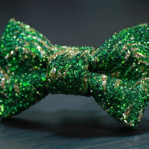 Op de afbeelding: Een groene en gouden glitterstrik. De strik is gemaakt van een zachte, glimmende stof.