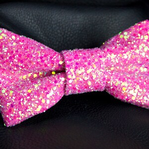 May include: A pink bow tie with iridescent glitter. The bow tie is made of a soft, textured fabric.