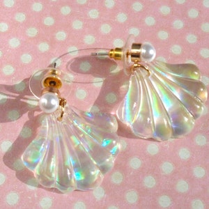 May include: A pair of iridescent seashell earrings with a pearl accent. The earrings are gold-toned and have a clear, iridescent finish.