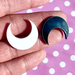 May include: Two crescent moon shapes, one in solid white and one in solid black, crafted from a smooth material. These two distinct moon-shaped pieces are presented side by side, showcasing a high-contrast design with clean, curved edges.