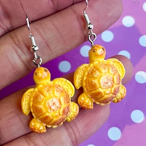 Op de afbeelding: Een paar oorbellen met kleine gele schildpadbedels. De schildpadden hebben gedetailleerde schilden en zijn opgehangen aan zilverkleurige oorhaken. Een helder, vrolijk accessoire.