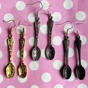 May include: A set of six spoon-shaped earrings. Two pairs are gold-toned and two pairs are silver-toned. The earrings are all in the shape of a spoon with a decorative handle.