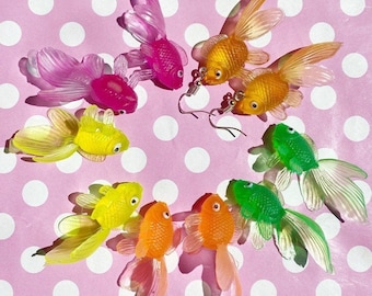Könnte beinhalten: Ein Set mit acht bunten Goldfisch-Ohrringen. Die Ohrringe sind aus Kunststoff und haben eine glänzende Oberfläche. Die Goldfische sind in verschiedenen Farben, darunter rosa, gelb, grün und orange.