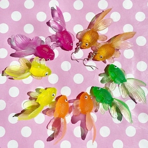 Könnte beinhalten: Ein Set mit acht bunten Goldfisch-Ohrringen. Die Ohrringe sind aus Kunststoff und haben eine glänzende Oberfläche. Die Goldfische sind in verschiedenen Farben, darunter rosa, gelb, grün und orange.