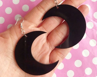 May include: A pair of black crescent moon earrings. The earrings are made of acrylic and have a shiny finish.