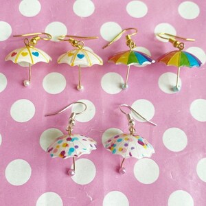 Könnte beinhalten: Ein Set mit sechs bunten Regenschirm-Ohrringen. Die Ohrringe sind aus Polymer Clay gefertigt und haben verschiedene Designs, darunter einen Regenbogen, Punkte und Herzen. Die Ohrringe sind perfekt, um jedem Outfit einen Hauch von Verspieltheit zu verleihen.