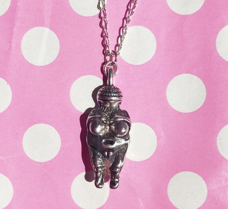 May include: A silver necklace with a pendant shaped like a woman. The pendant is detailed and has a textured surface.