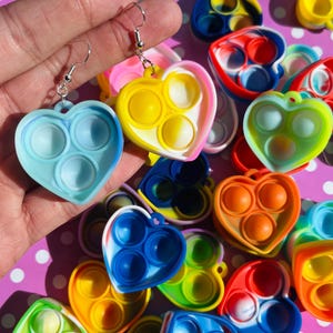 May include: Heart-shaped earrings in various colors, featuring a bubble-popping design. The earrings are in shades of blue, yellow, pink, orange, and green. The earrings have a silver hook. The image shows multiple earrings.