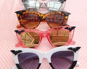 Puede incluir: Cuatro pares de gafas de sol de ojo de gato con detalles de murciélago. Las gafas de sol son de cuatro colores diferentes: plateado, marrón, rosa y blanco. Las lentes son espejadas o tintadas.
