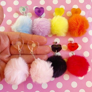 Könnte beinhalten: Ein Set mit acht Paar Ohrringen mit einem Bommel-Anhänger und einem herzförmigen Anhänger. Die Bommel sind in verschiedenen Farben erhältlich, darunter rosa, blau, lila, gelb, orange, rot, schwarz und weiß. Die herzförmigen Anhänger sind aus klarem Kunststoff und haben verschiedene Farben, darunter lila, gelb, orange und rot.