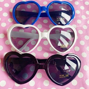 May include: Three pairs of heart-shaped sunglasses. The top pair is blue, the middle pair is white, and the bottom pair is black. All three pairs have UV 400 protection.
