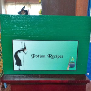 May include: A green wooden box with a label that says "Potion Recipes". The label features a cartoon witch and a cauldron with a broom.