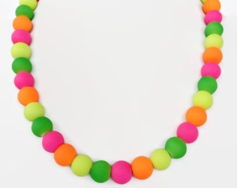 May include: A colorful necklace made of bright green, pink, and orange beads. The beads are round and smooth, and they are strung together on a clear string.