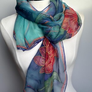 May include: A sheer silk scarf with a floral design. The scarf features a color palette of teal, navy, and red, with gold accents. The scarf is draped over a white mannequin, showcasing its flowing fabric and intricate details.