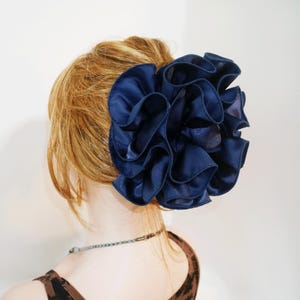 以下が含まれることがあります： 濃い青色の布製の大きな花のヘアクリップ。花は複数の層のフリル生地で作られています。