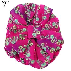 May include: A pink fabric hair bow with a floral pattern and a gradient from pink to purple. The bow is decorated with small, shiny embellishments.