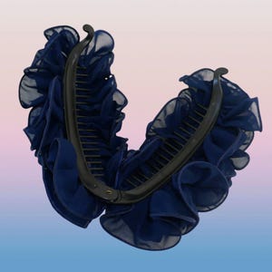 May include: A navy blue banana hair clip featuring a curved black plastic comb base adorned with layers of ruffled, sheer fabric. The two sides of the hair accessory are connected by a small metal hinge at the bottom, creating a V-shaped opening.