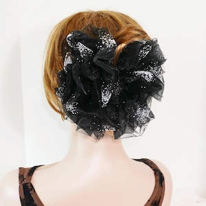 May include: A black hair accessory with silver glitter. The accessory is made of tulle and is shaped like a flower.