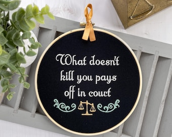 What doesn't kill you pays off in court: Finished embroidery hoop art. Funny lawyer gift for women or personal injury attorney office decor.