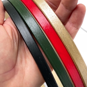 May include: Four wooden embroidery hoops in different colors: gold, red, green, and black. The hoops are stacked on top of each other.