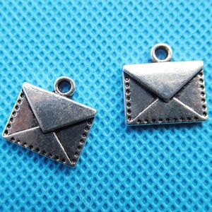May include: Two silver-toned metal envelope charms with a decorative border. The charms have a loop at the top for attaching to a necklace or bracelet.