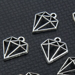 May include: Ten silver-toned diamond-shaped charms with a geometric design. The charms have a hole at the top for attaching to jewellery.