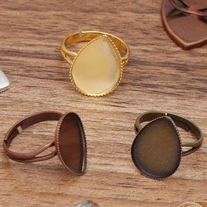 Könnte beinhalten: Sortiment an tropfenförmigen Ringrohlingen mit verschiedenen Metalloberflächen, darunter Gold, Silber, Bronze und Kupfer. Die Rohlinge sind bereit, mit Harz, Farbe oder anderen Verzierungen individuell gestaltet zu werden.