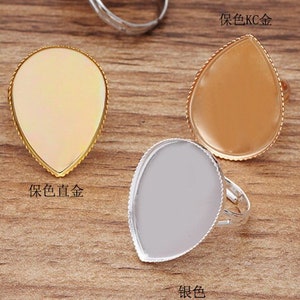 Könnte beinhalten: Sortiment von sechs tropfenförmigen Ringrohlingen in verschiedenen Metalloberflächen: Antikbronze, Roségold, Silber, Gold und zwei Goldtönen. Die Ringrohlinge sind bereit für die individuelle Gestaltung mit Harz, Farbe oder anderen Verzierungen.