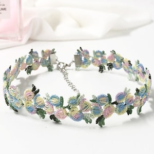 May include: A delicate floral choker necklace with a silver chain and clasp. The choker is made of a soft, embroidered fabric with pastel blue, pink, and yellow flowers.