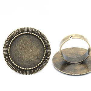 Può includere: Un'impostazione per anello dorata con una lunetta rotonda, perfetta per aggiungere un ciondolo o una pietra personalizzata. L'anello è regolabile e ha un bordo testurizzato.