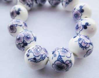 May include: A strand of white ceramic beads with a blue and pink floral design. The beads are round and have a glossy finish.