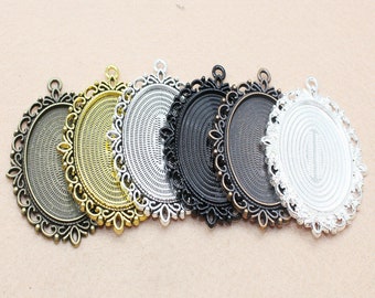May include: Six oval-shaped metal pendant trays with ornate filigree edges. The trays are in various finishes: antique bronze, gold, silver, black, and white.