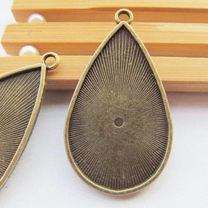 Könnte beinhalten: Zwei antike goldfarbene Metall-Anhänger in Tropfenform mit strukturierter Oberfläche. Die Anhänger haben oben eine kleine Öse zum Anbringen einer Kette oder Schnur.