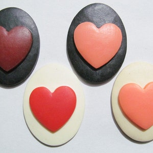 May include: Four heart-shaped buttons, two on black backgrounds and two on white backgrounds. The hearts are red, pink, and a darker shade of red.