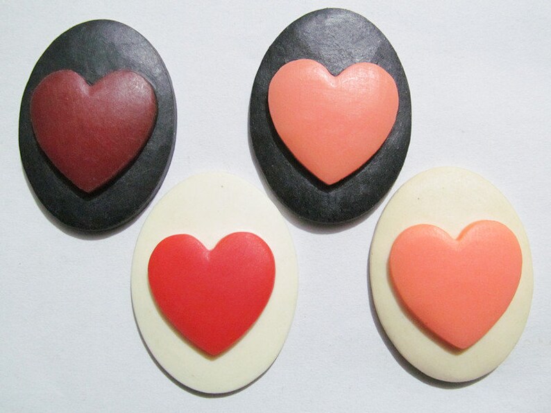 May include: Four heart-shaped buttons, two on black backgrounds and two on white backgrounds. The hearts are red, pink, and a darker shade of red.