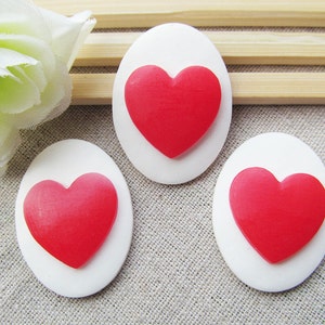 May include: Three white oval-shaped cabochons with red heart-shaped embellishments.
