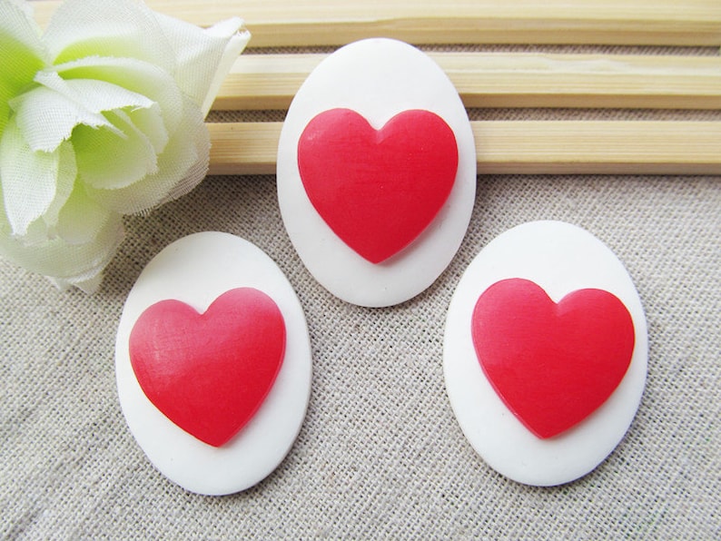 May include: Three white oval-shaped cabochons with red heart-shaped embellishments.