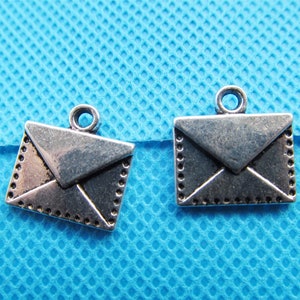 May include: Two silver-toned envelope charms with a decorative border. The charms have a loop at the top for attaching to a necklace or bracelet.