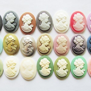 May include: Assortment of 20 oval-shaped cameo-style resin cabochons in various colors, including white, pink, blue, green, gold, and silver. Each cabochon features a raised design of a woman's profile.