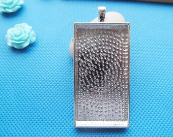 May include: Silver-toned pendant tray with a rectangular shape and a textured surface. The tray is designed to hold a small image or other decorative element.