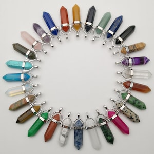May include: A collection of 24 gemstone point pendants with silver-toned bail loops. The pendants are arranged in a circle, with each pendant featuring a different color and type of gemstone.