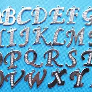 Puede incluir: Un conjunto de 26 abalorios de letras del alfabeto de metal plateado con detalles de diamantes de imitación transparentes. Cada letra está hecha individualmente y presenta un diseño único.