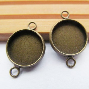 Puede incluir: Dos colgantes de metal bronce antiguo con inserciones redondas de vidrio cabujón. Los ajustes tienen un bucle en la parte superior para sujetar a una cadena o cordón.