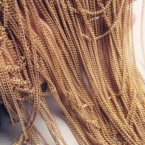 May include: A close-up of a bundle of gold-colored chain links. The chains are arranged in a cascading pattern, creating a textured and shimmering effect.