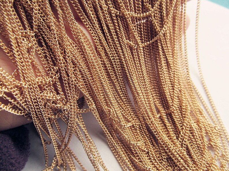 May include: A close-up of a bundle of gold-colored chain links. The chains are arranged in a cascading pattern, creating a textured and shimmering effect.