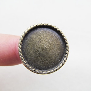 Può includere: Un anello rotondo in metallo color bronzo con un bordo a forma di corda. L'anello è liscio e ha una superficie liscia.
