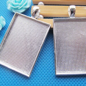 May include: Two silver-toned metal pendant trays with a textured surface. The trays are rectangular and have a loop at the top for hanging.